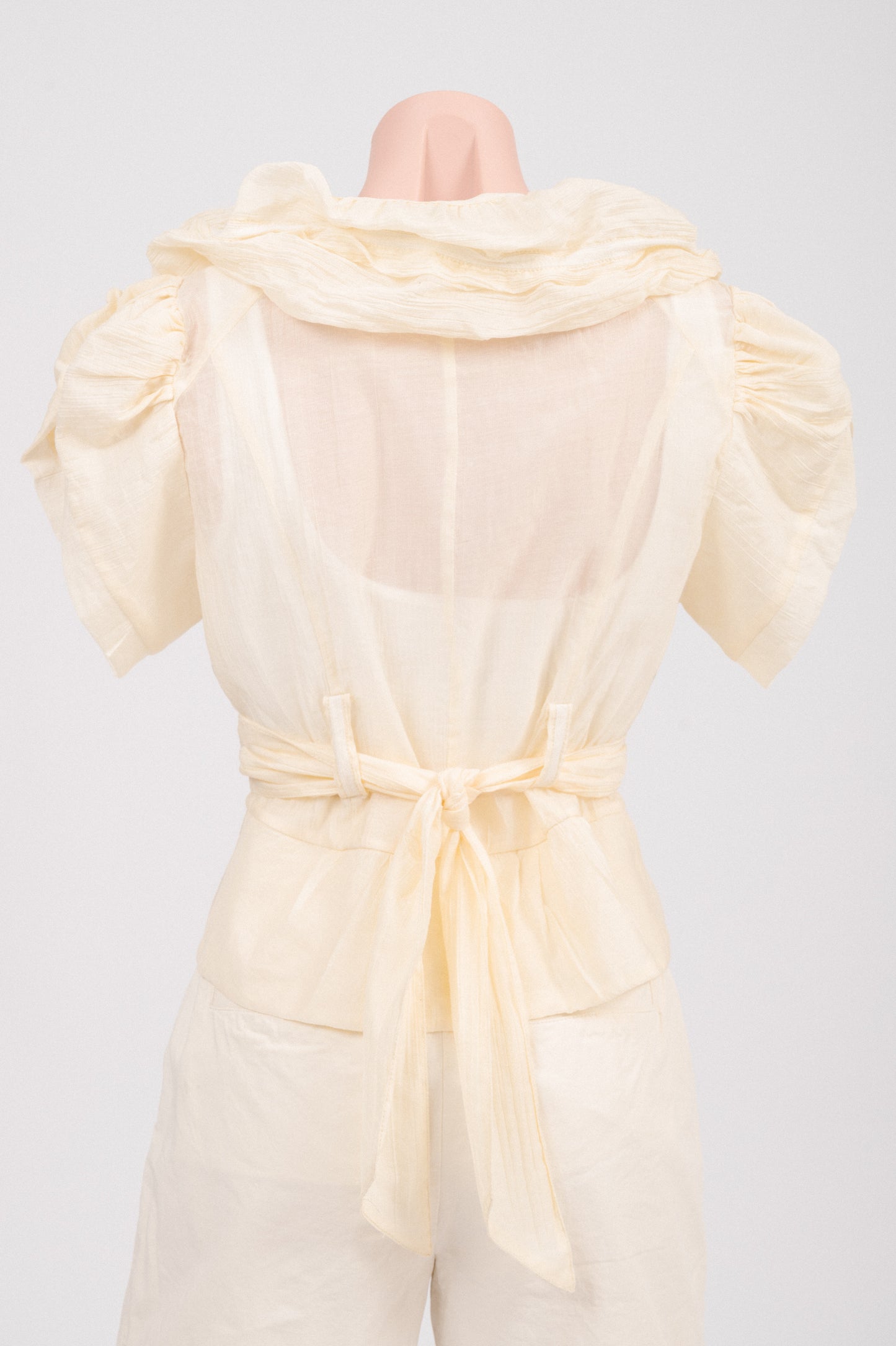 Back view of vintage butter yellow blouse showing curved high-low hem and ruffle panel.