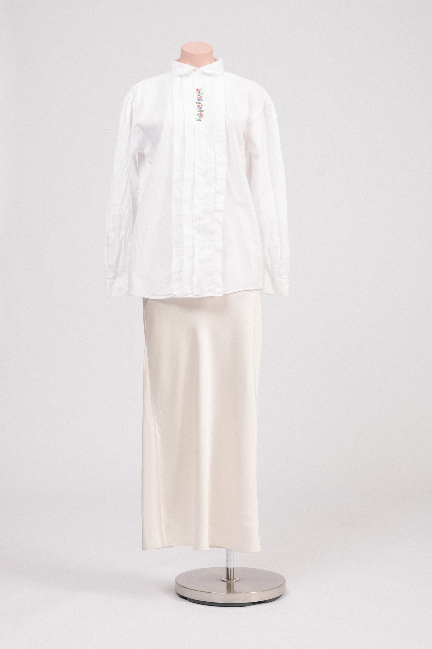 Vintage white cotton blouse with floral embroidery and concealed button placket photographed front-on against a neutral background.