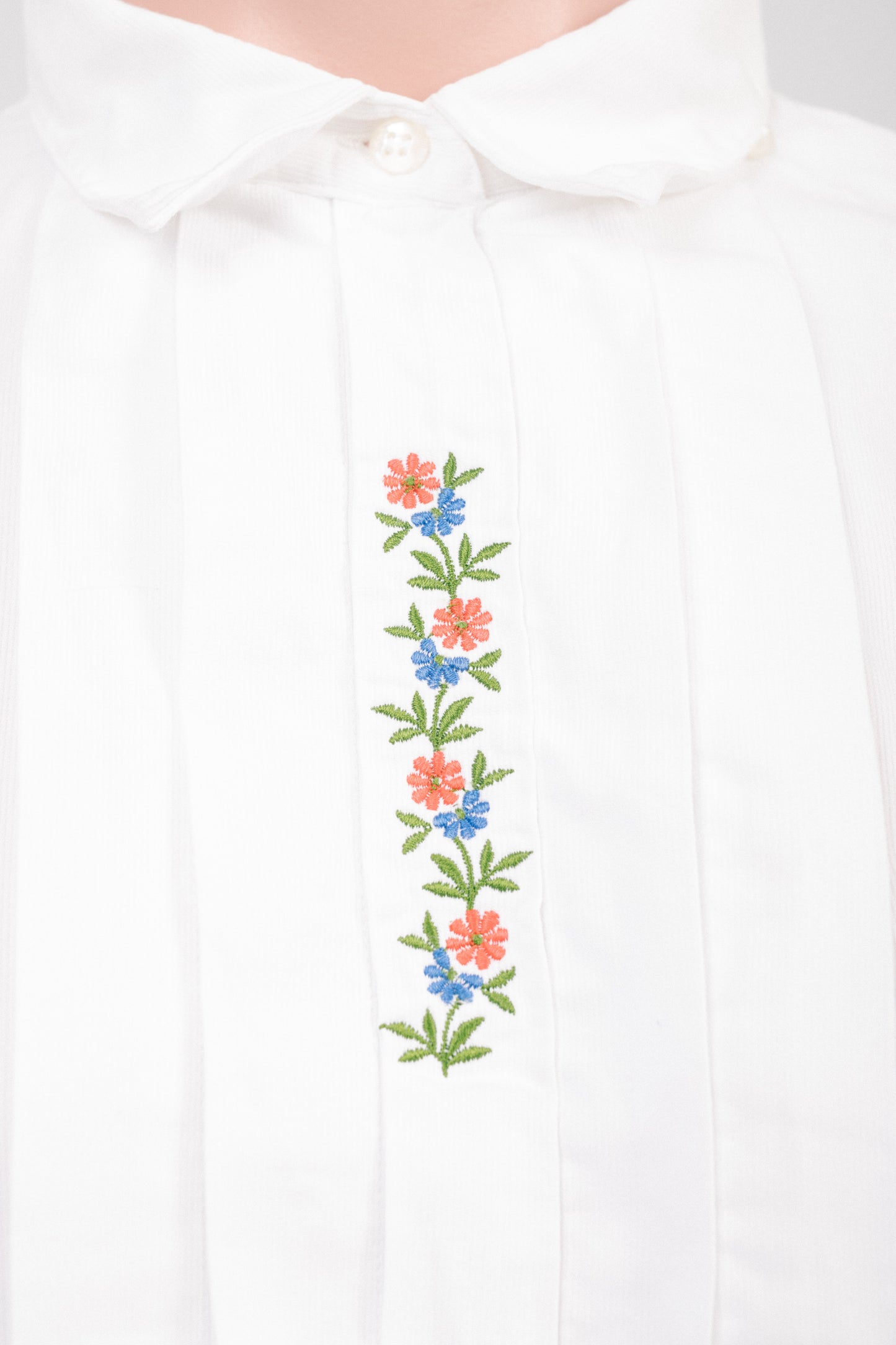 Close-up of floral embroidery and concealed button placket on vintage white cotton blouse showing ribbed fabric texture and heirloom detailing.